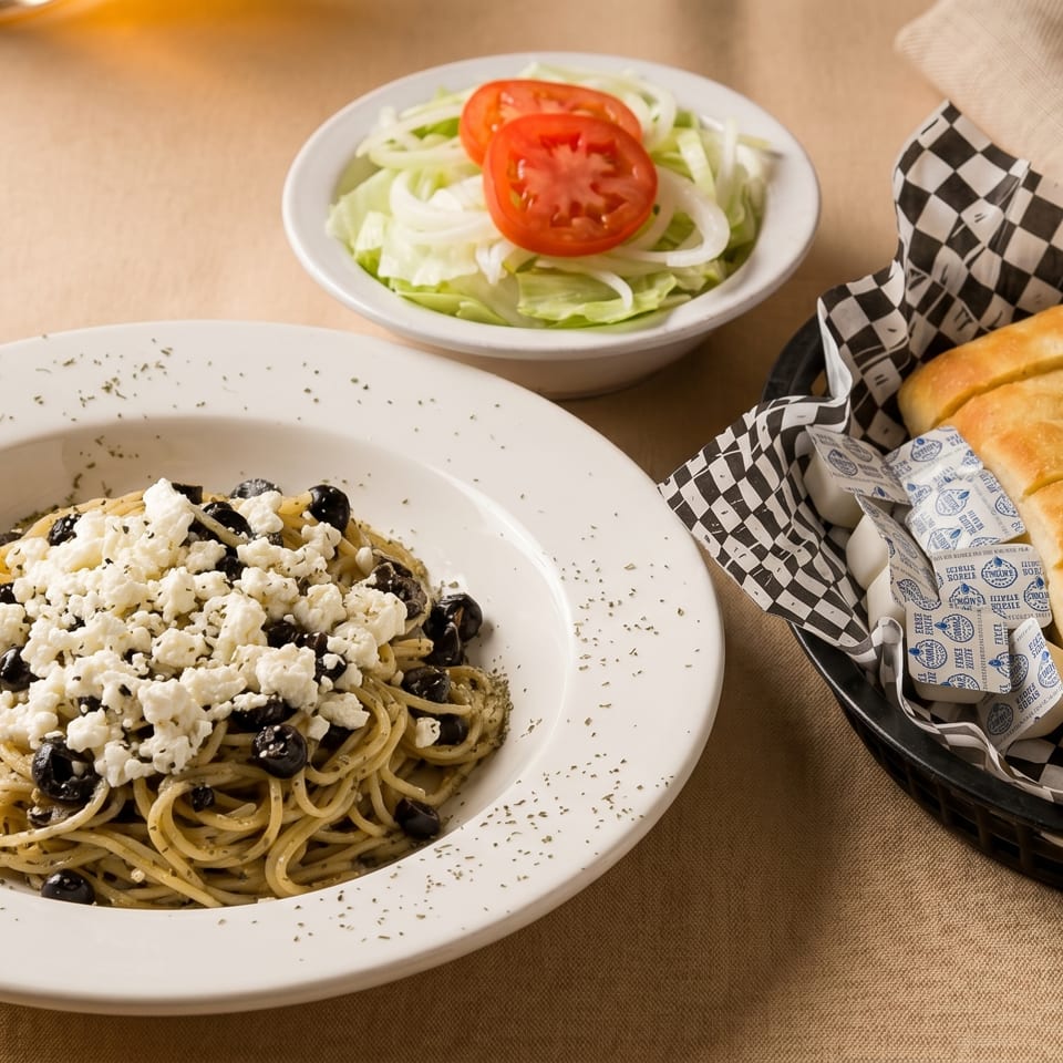 Spaghetti with feta and olives, a side salad, and garlic bread in a basket.