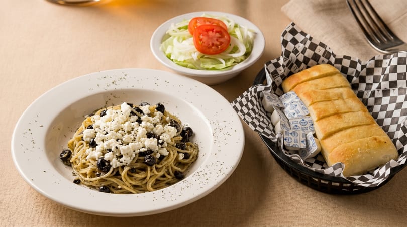 Spaghetti with feta and olives, a side salad, and garlic bread in a basket.