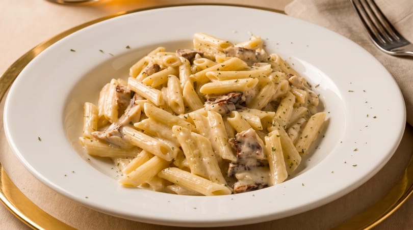 Creamy mushroom penne pasta in a white bowl, garnished with herbs, on a gold-rimmed plate.