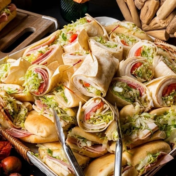 A large platter filled with an assortment of sandwiches and wraps, garnished with autumn leaves.