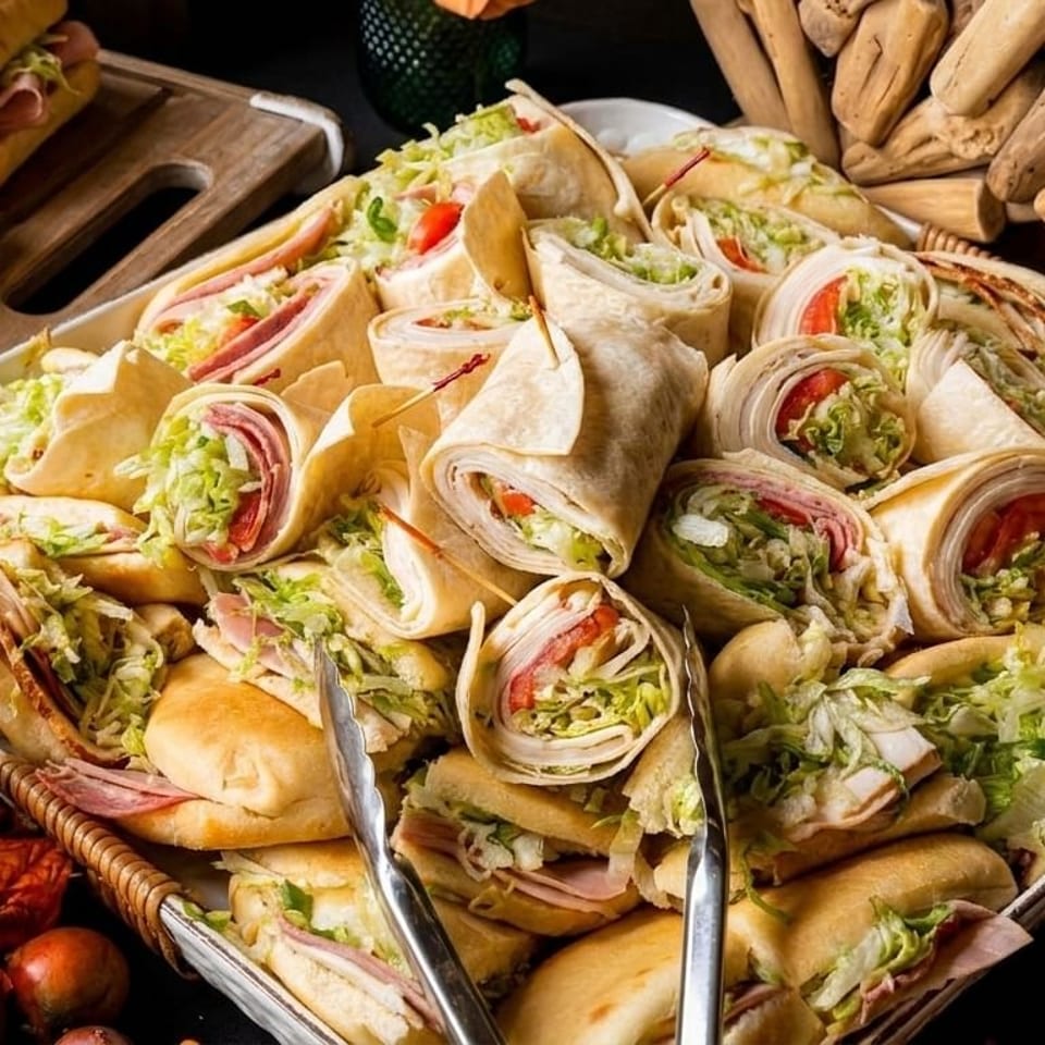 A large platter filled with an assortment of sandwiches and wraps, garnished with autumn leaves.