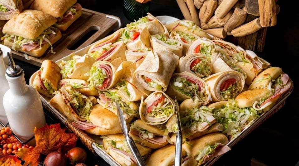 A large platter filled with an assortment of sandwiches and wraps, garnished with autumn leaves.