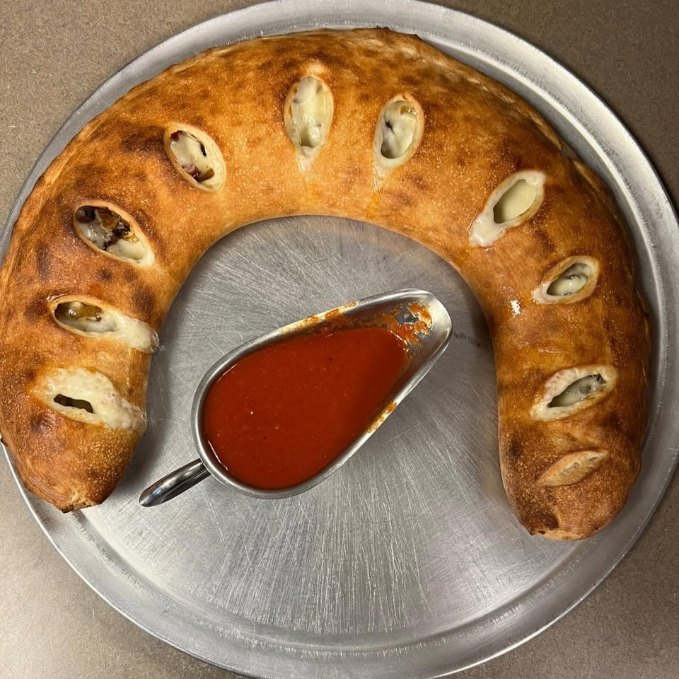 A crescent-shaped calzone with visible cheese and fillings, served with a side of marinara sauce.