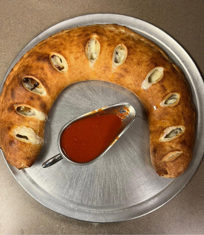 A crescent-shaped calzone with visible cheese and fillings, served with a side of marinara sauce.